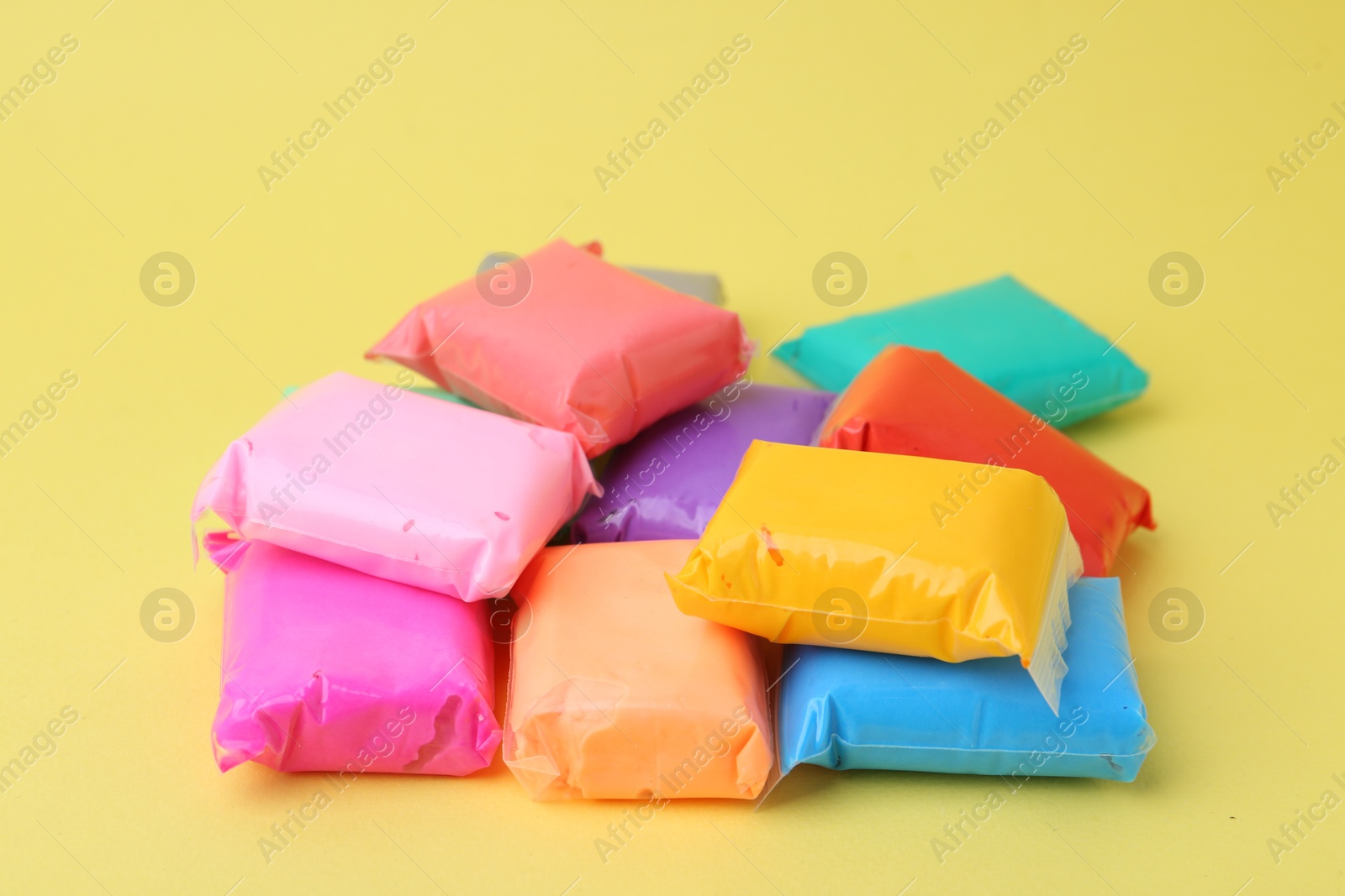 Photo of Different colorful play dough in packages on yellow background, closeup