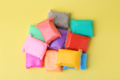 Photo of Different colorful play dough in packages on yellow background, top view