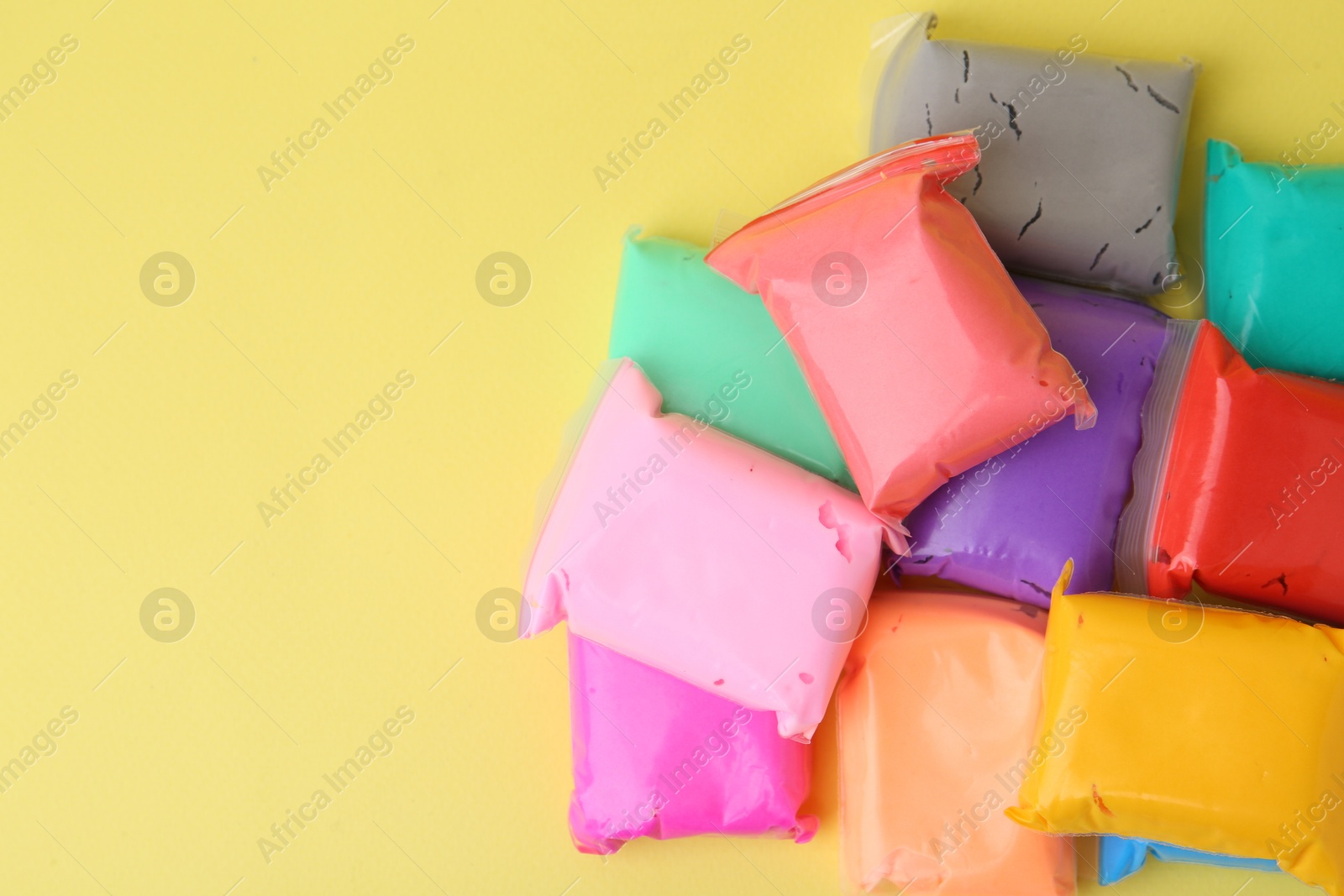 Photo of Different colorful play dough in packages on yellow background, top view. Space for text