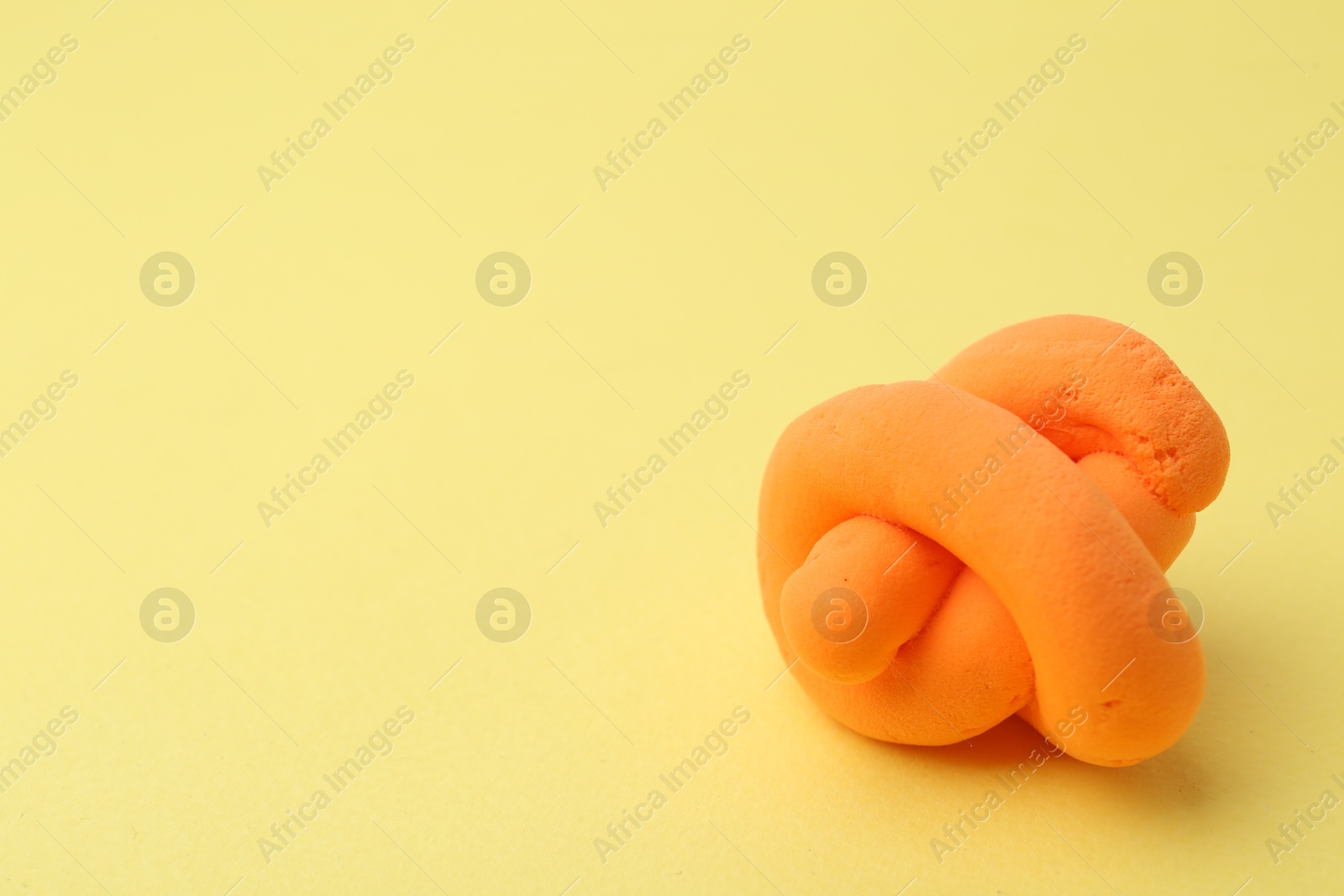 Photo of Orange play dough on yellow background, closeup. Space for text