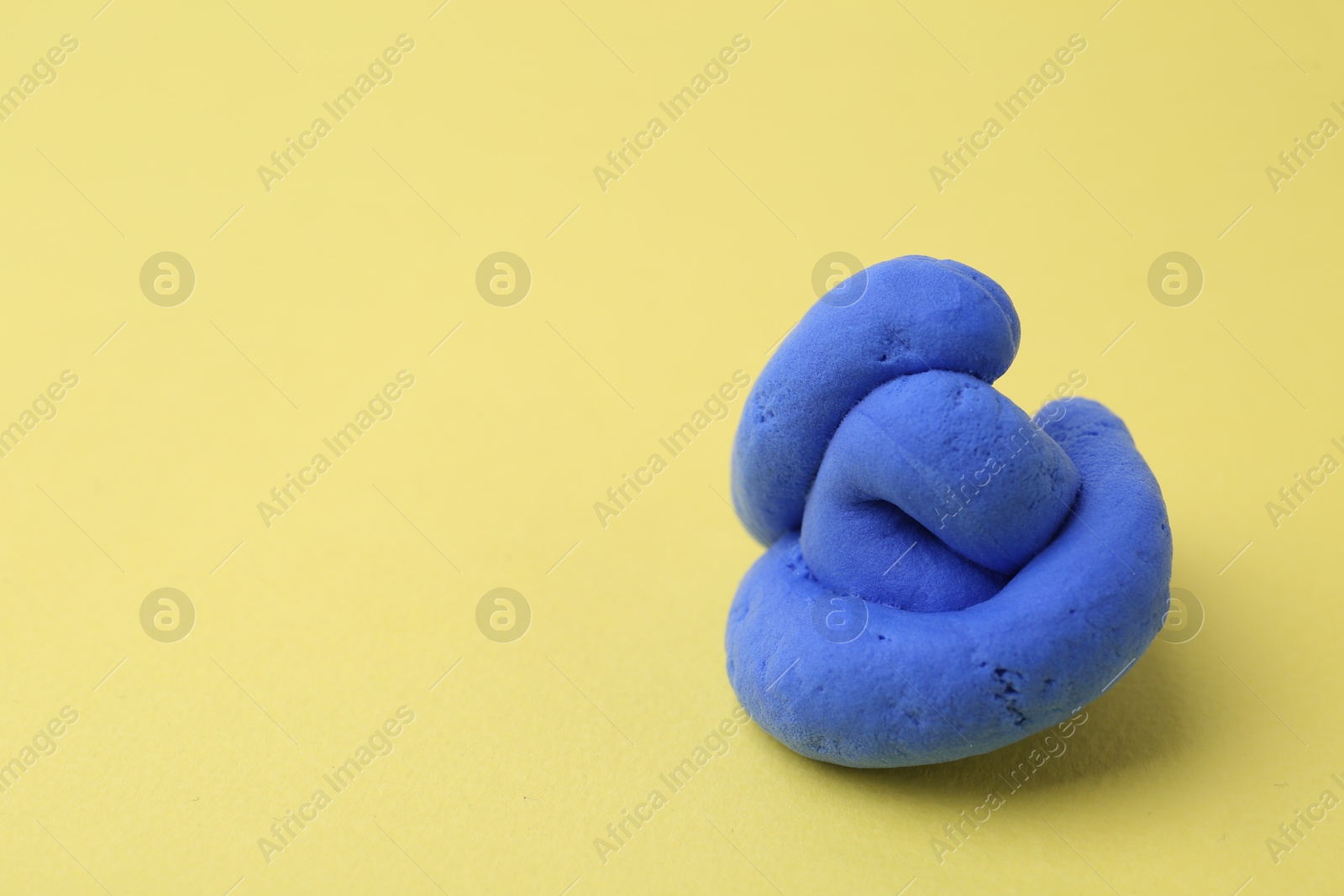 Photo of Bright blue play dough on yellow background, space for text