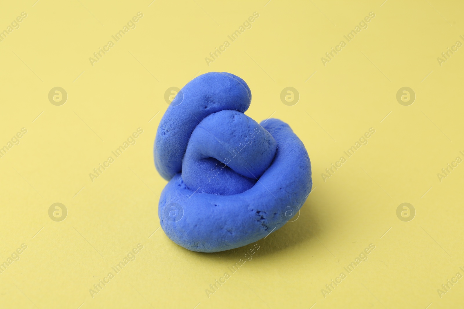 Photo of Bright blue play dough on yellow background, closeup