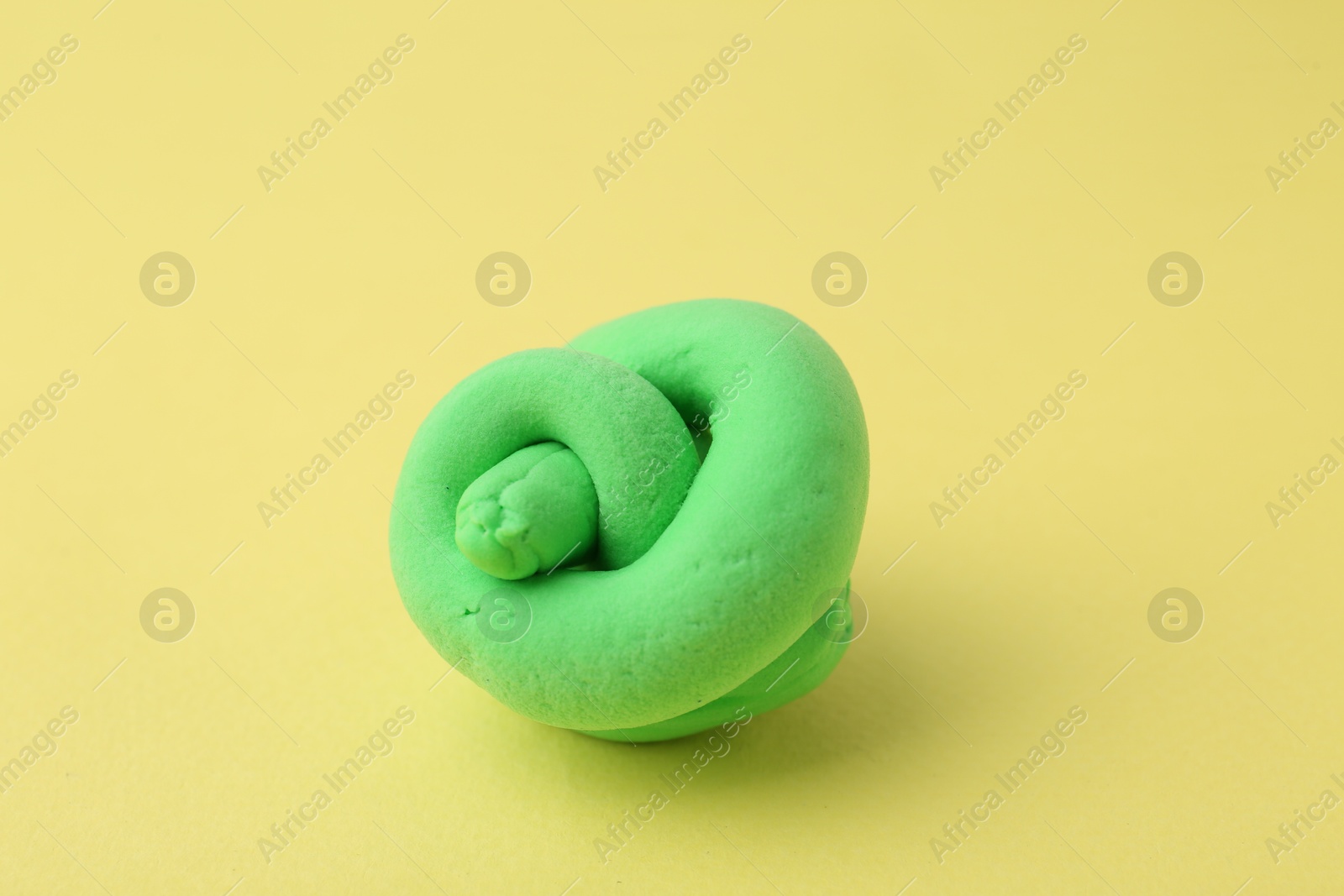 Photo of Bright green play dough on yellow background, closeup