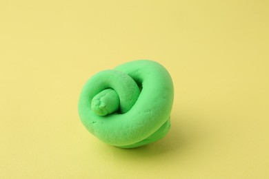 Photo of Bright green play dough on yellow background, closeup