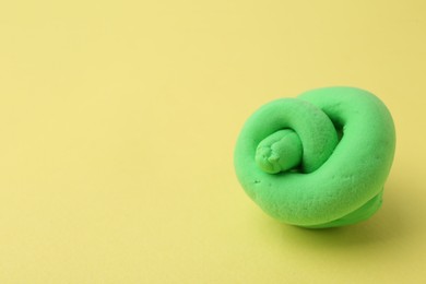 Photo of Bright green play dough on yellow background, closeup. Space for text