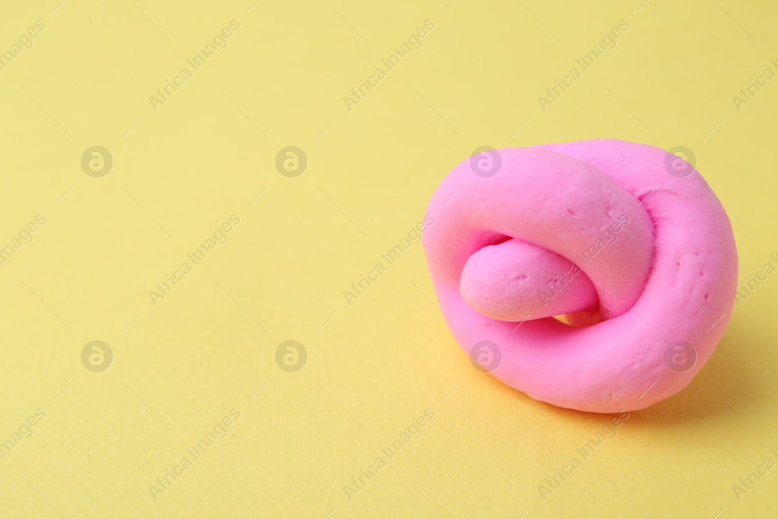 Photo of Bright pink play dough on yellow background, closeup. Space for text