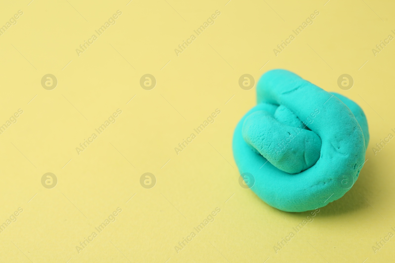 Photo of Bright turquoise play dough on yellow background, closeup. Space for text