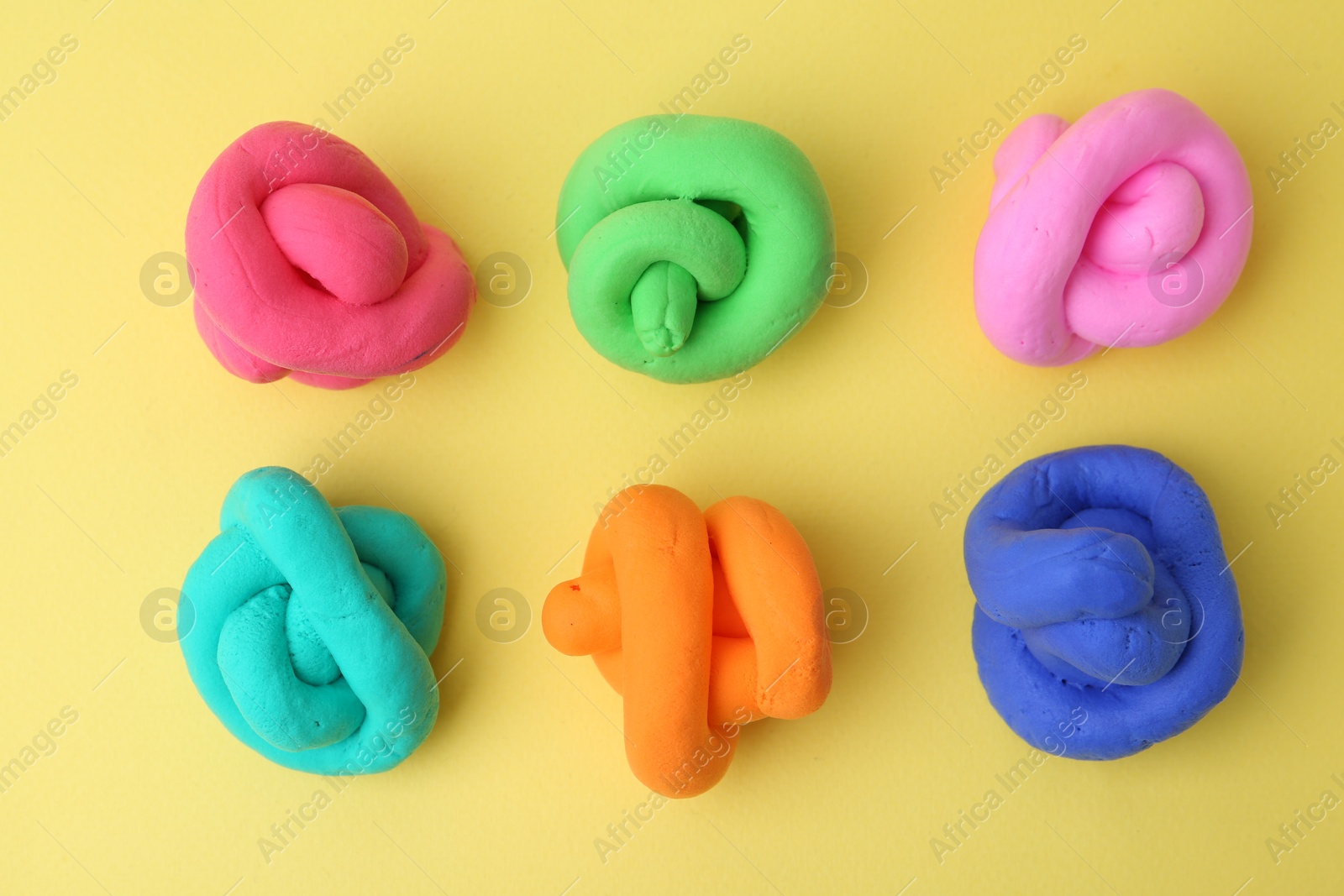 Photo of Different colorful play dough on yellow background, flat lay