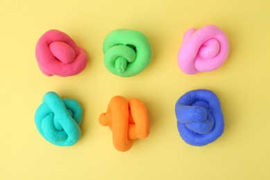 Photo of Different colorful play dough on yellow background, flat lay