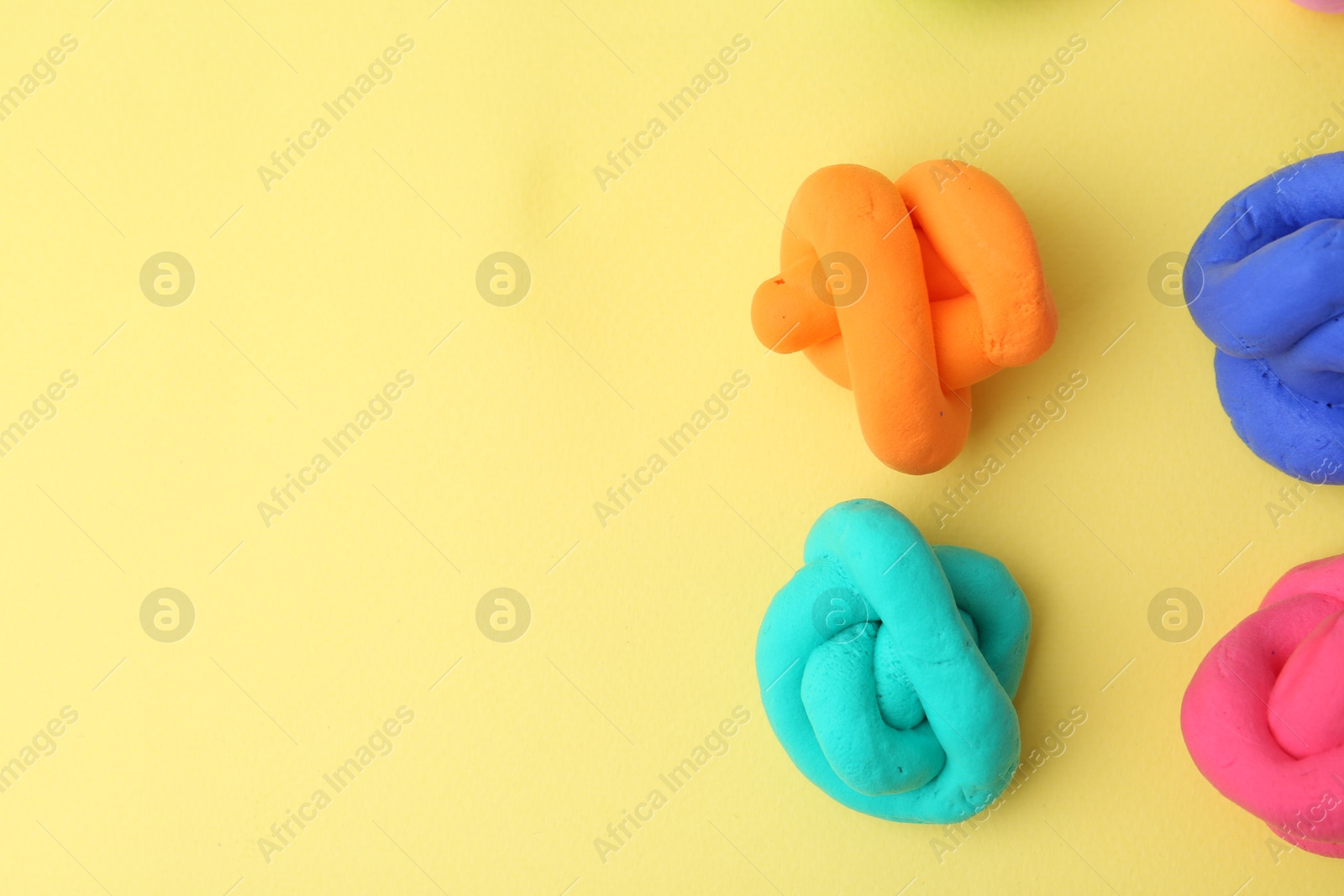 Photo of Different colorful play dough on yellow background, flat lay. Space for text