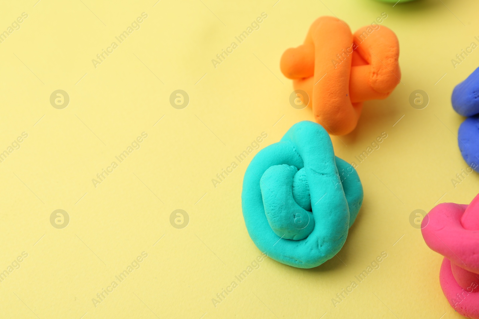 Photo of Different colorful play dough on yellow background, closeup. Space for text