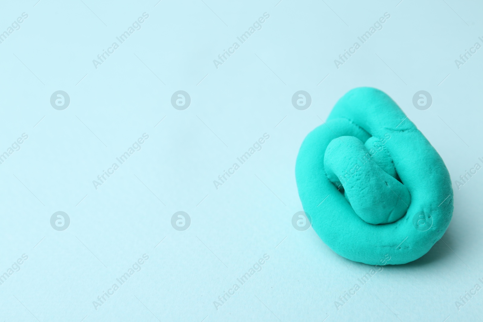 Photo of Turquoise play dough on light blue background, closeup. Space for text