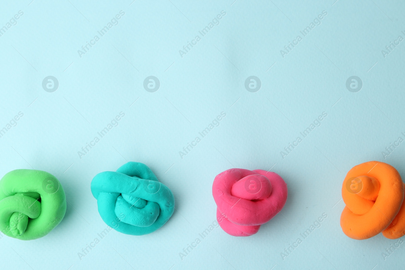 Photo of Different colorful play dough on light blue background, flat lay. Space for text