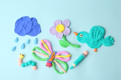 Photo of Different colorful child's crafts made of play dough on light blue background, flat lay