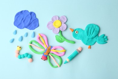 Photo of Different colorful child's crafts made of play dough on light blue background, flat lay