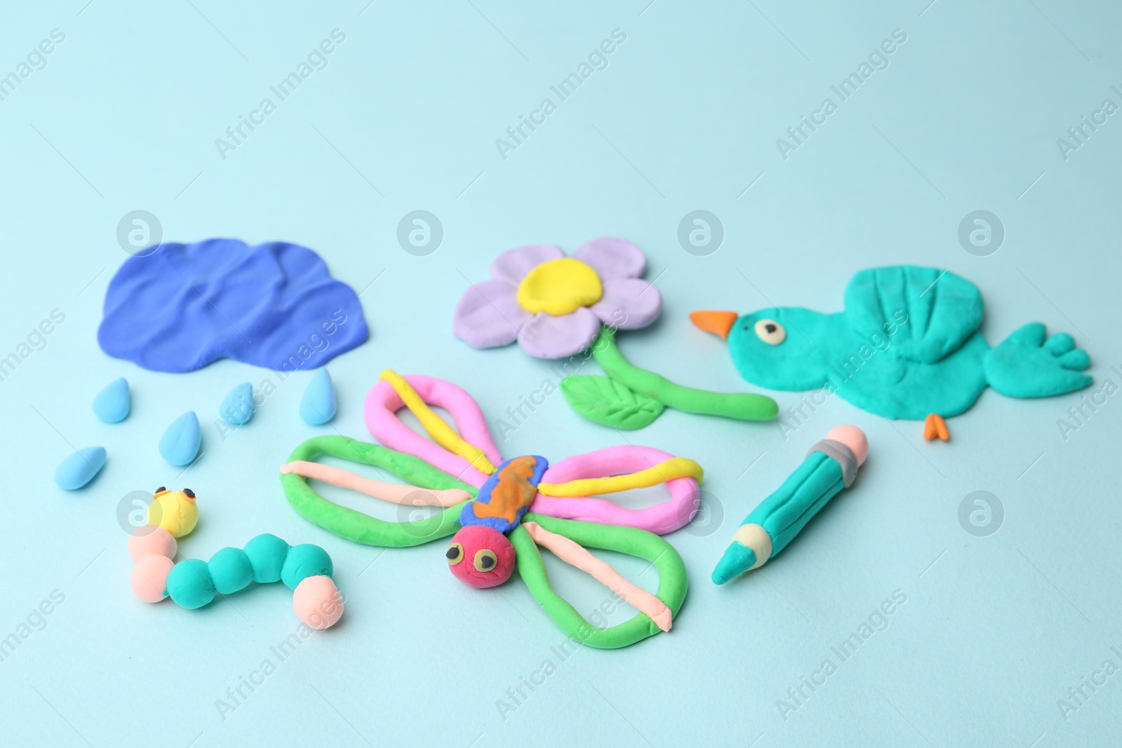 Photo of Different colorful child's crafts made of play dough on light blue background, closeup