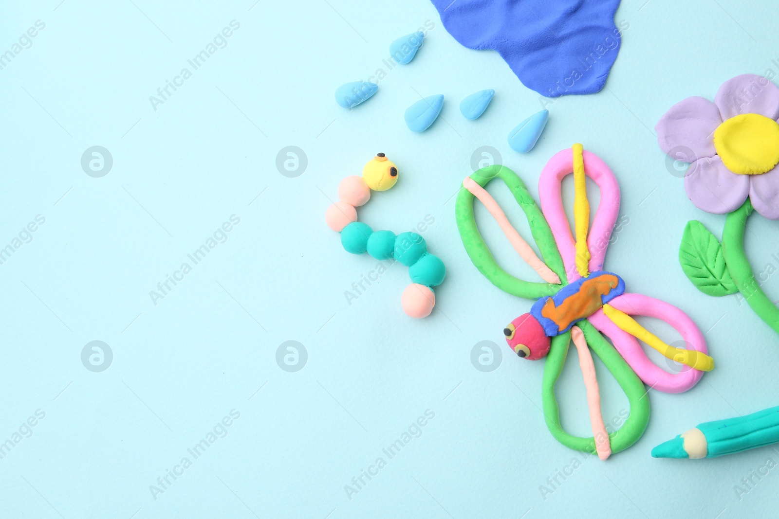 Photo of Different colorful child's crafts made of play dough on light blue background, flat lay. Space for text