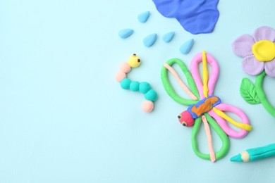 Photo of Different colorful child's crafts made of play dough on light blue background, flat lay. Space for text