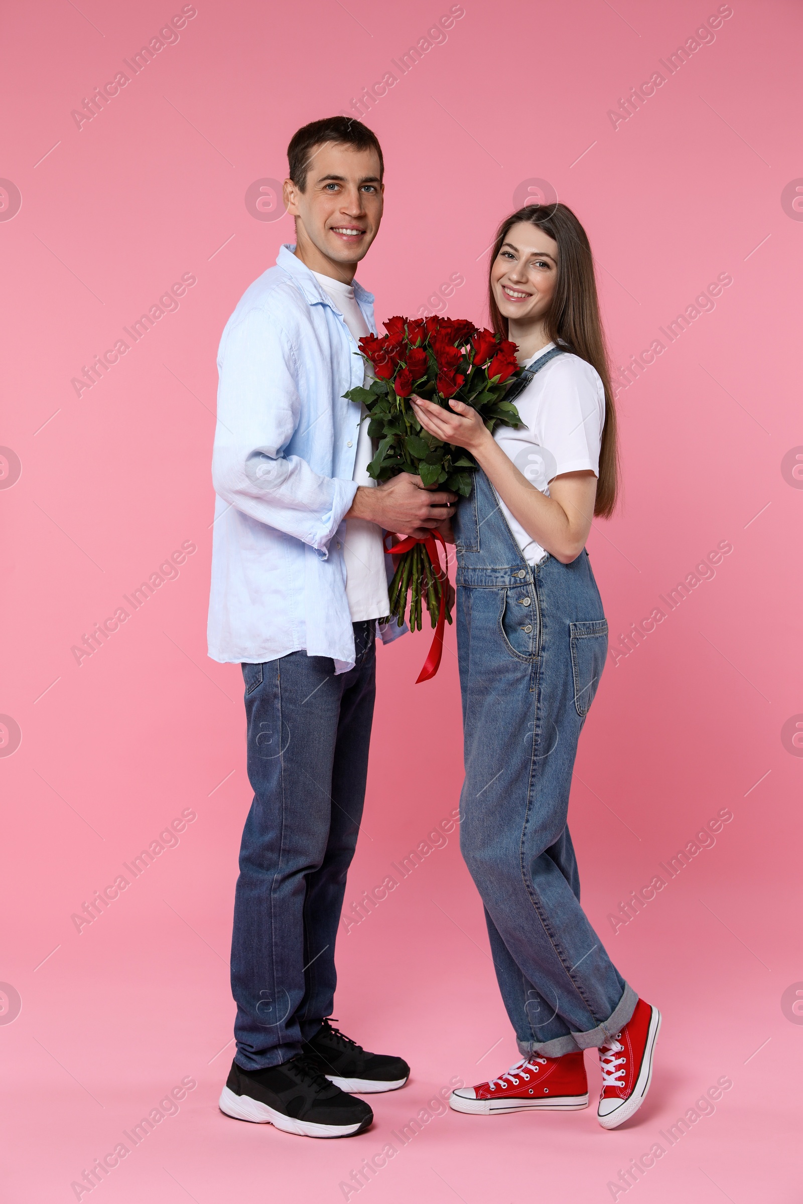 Photo of Lovely couple with bouquet of red roses on pink background. Valentine's day celebration