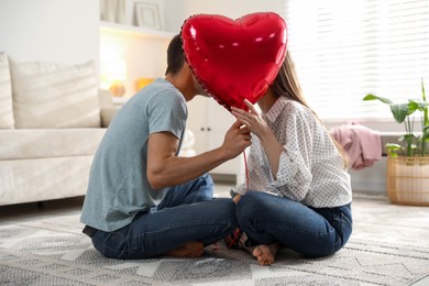 Photo of Lovely couple kissing behind heart shaped balloon indoors. Valentine's day celebration