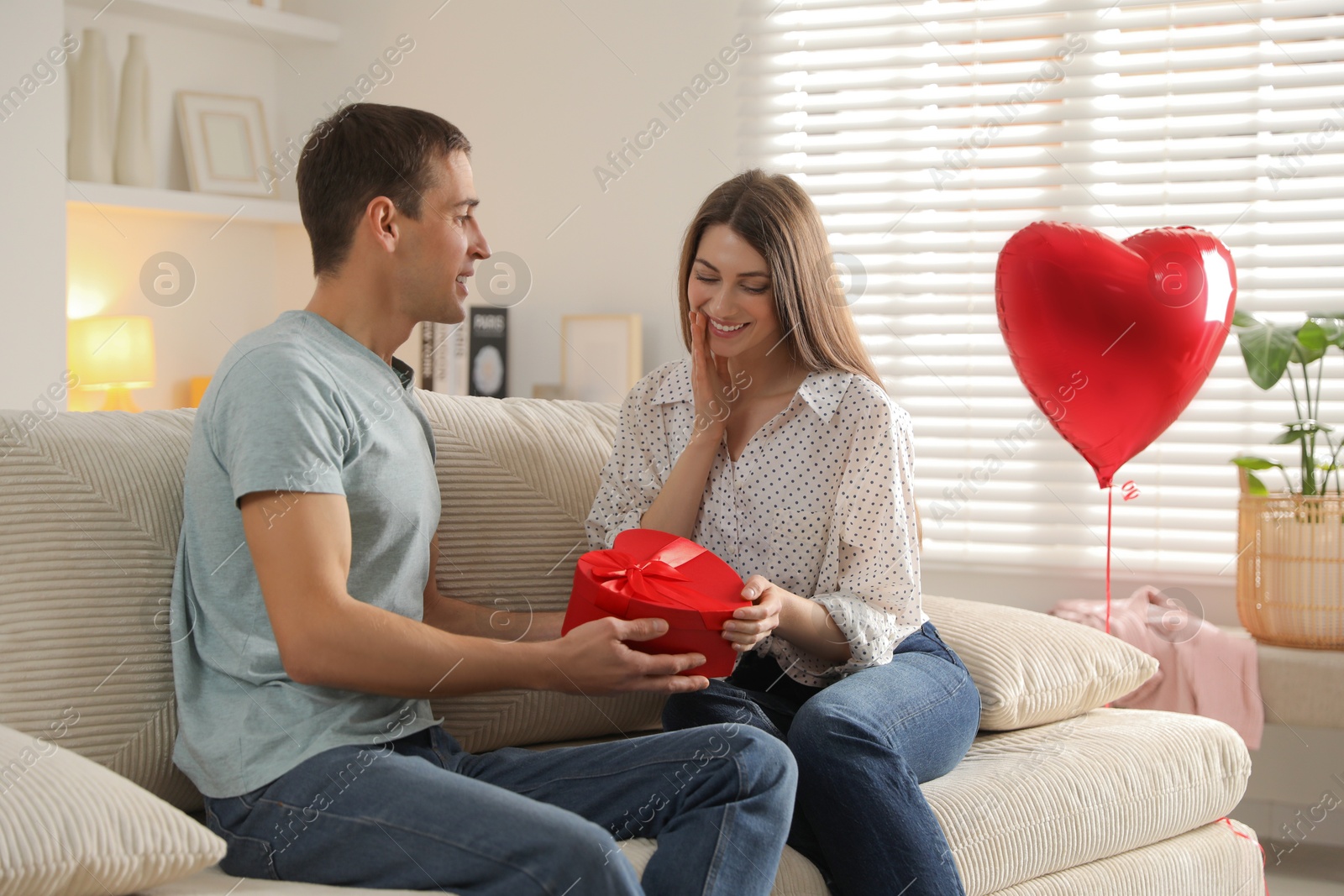 Photo of Lovely man surprising his girlfriend with Valentine's day gift indoors