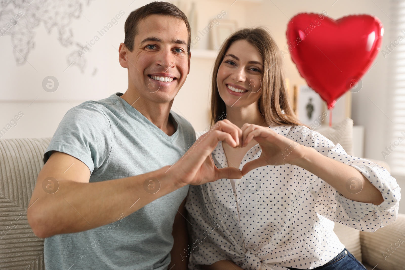 Photo of Lovely couple making heart with hands indoors. Valentine's day celebration