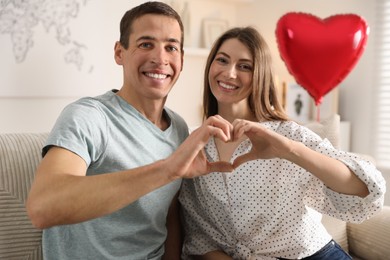 Photo of Lovely couple making heart with hands indoors. Valentine's day celebration