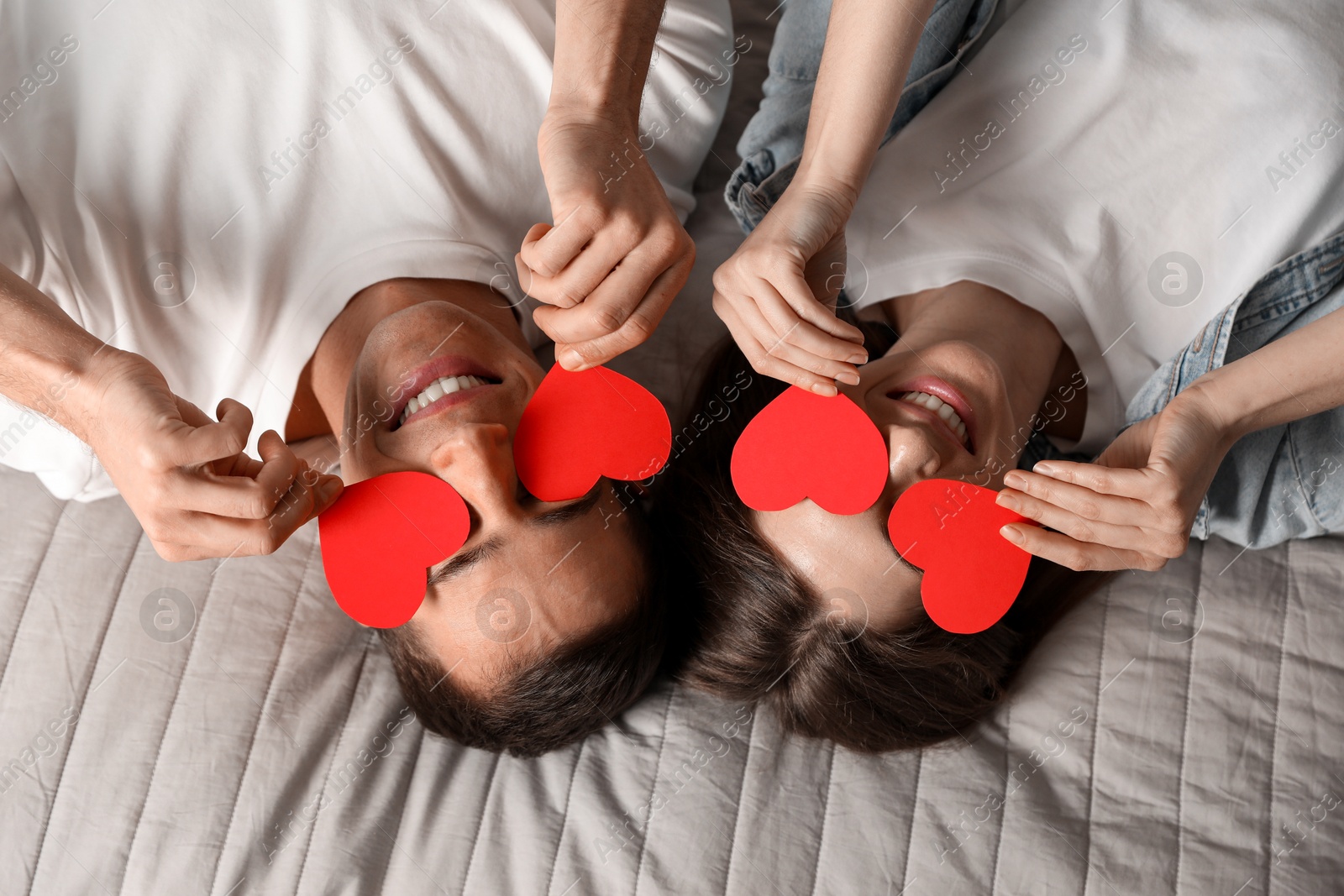 Photo of Lovely couple with paper hearts on bed, top view. Valentine's day celebration