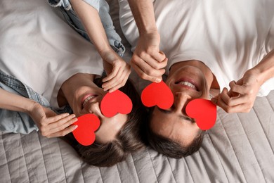 Photo of Lovely couple with paper hearts on bed, top view. Valentine's day celebration