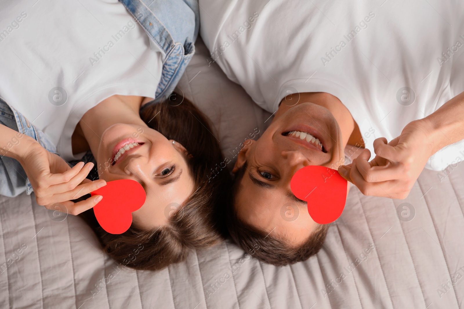 Photo of Lovely couple with paper hearts on bed, top view. Valentine's day celebration