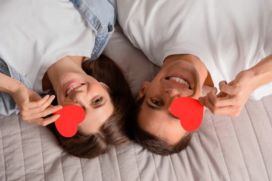 Photo of Lovely couple with paper hearts on bed, top view. Valentine's day celebration