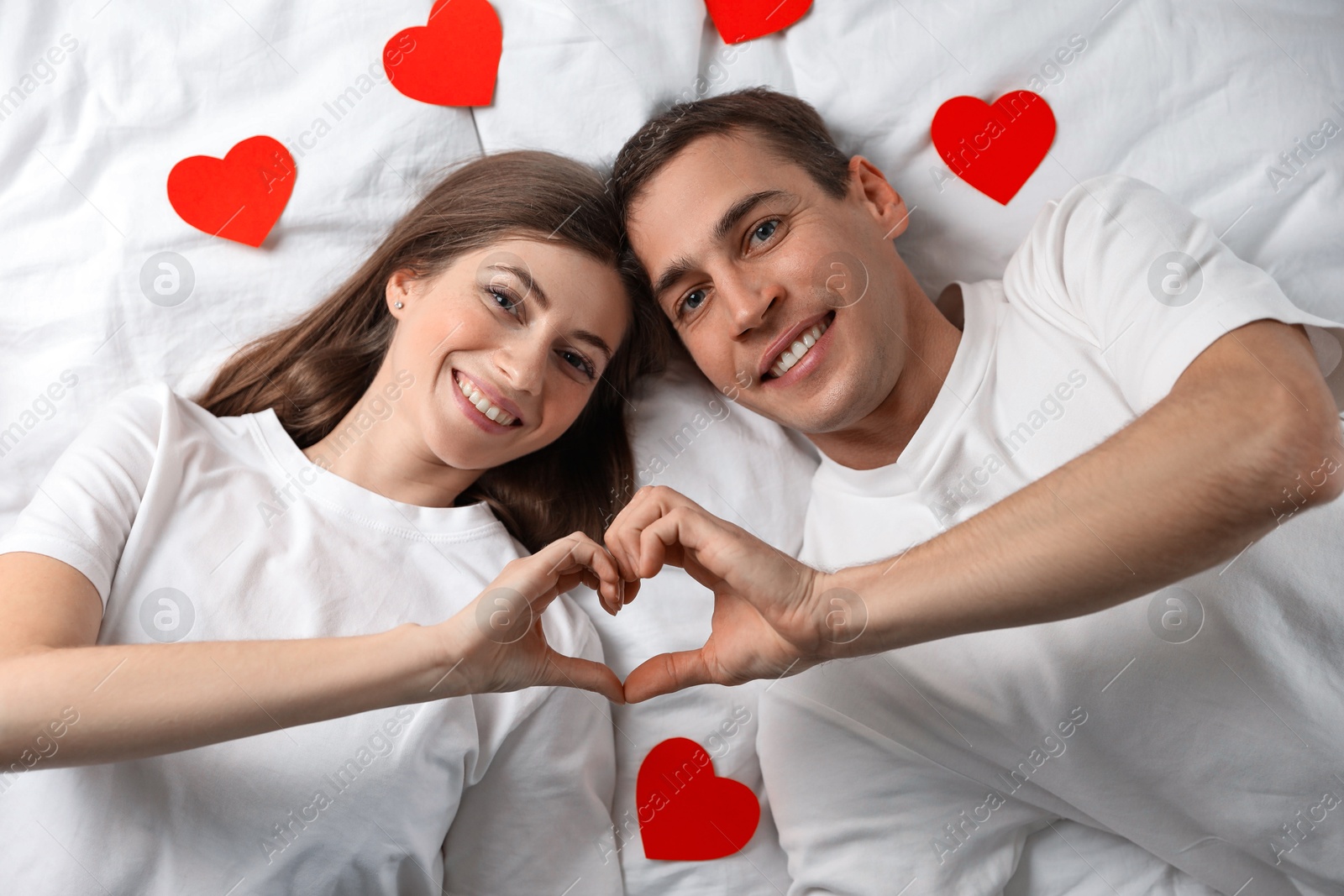 Photo of Lovely couple making heart with hands on bed, top view. Valentine's day celebration