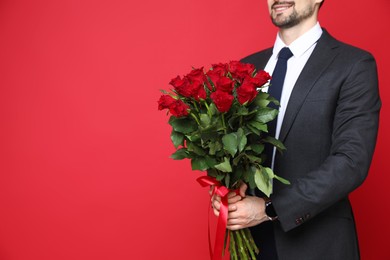 Photo of Happy Valentine's Day. Man with bouquet of roses on red background, closeup. Space for text