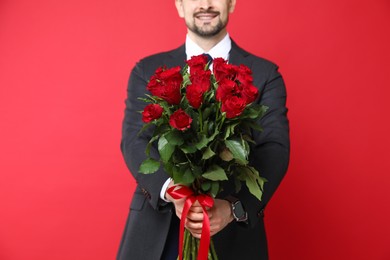 Photo of Happy Valentine's Day. Man with bouquet of roses on red background, closeup