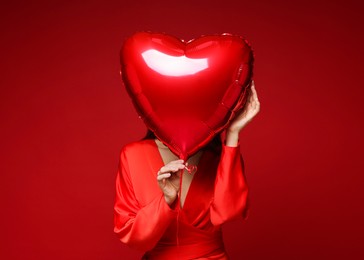 Photo of Happy Valentine's Day. Woman hiding behind heart shaped balloon on red background