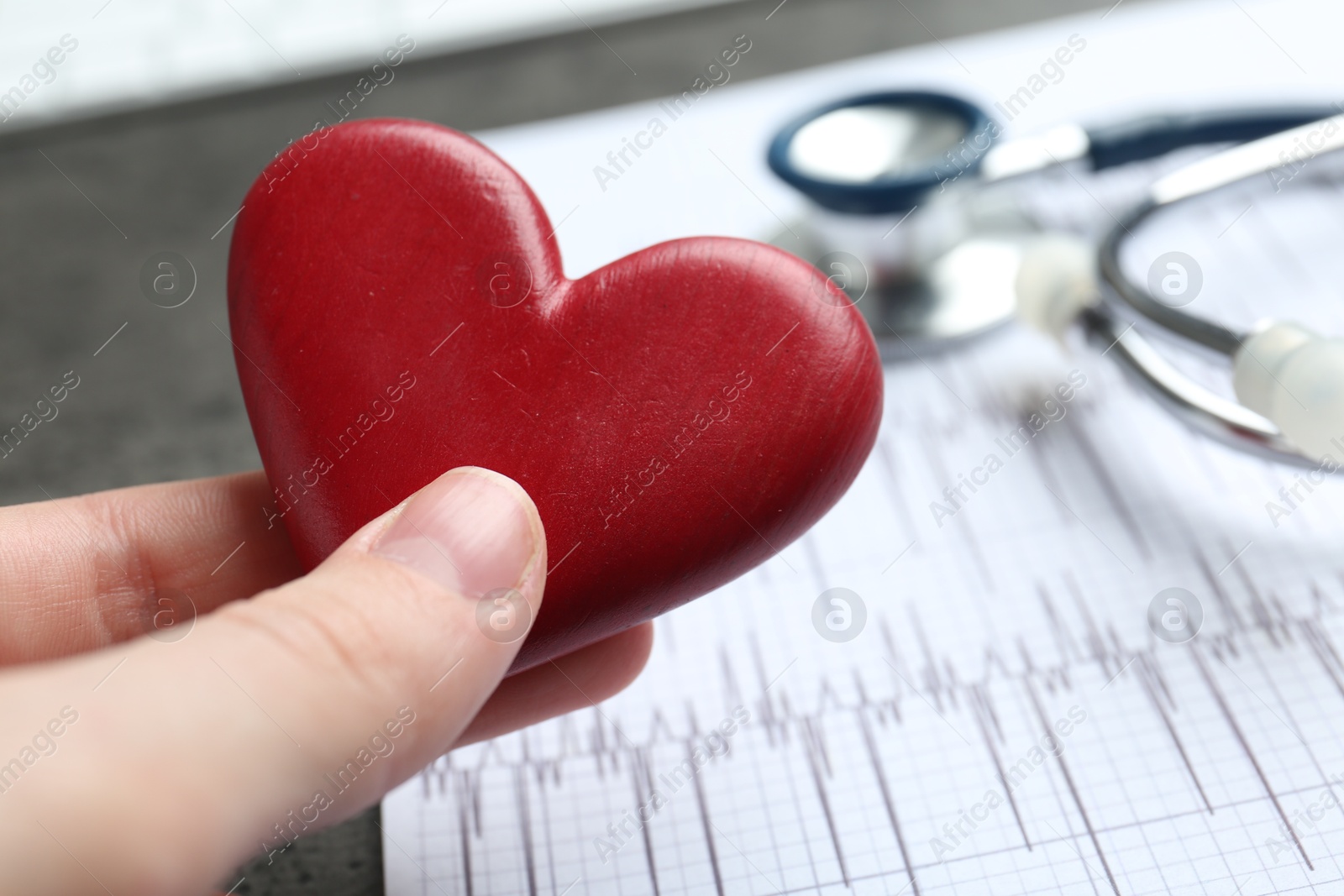 Photo of Cardiology. Woman with red decorative heart at gray table, closeup