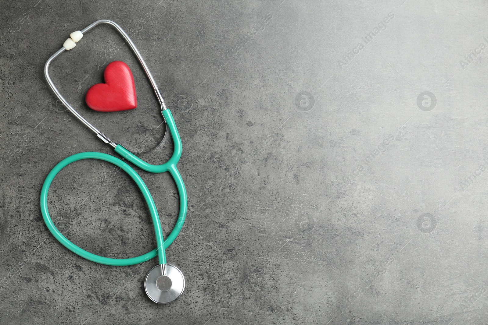 Photo of Cardiology. Stethoscope and red decorative heart on gray textured background, flat lay. Space for text