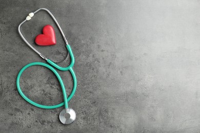 Photo of Cardiology. Stethoscope and red decorative heart on gray textured background, flat lay. Space for text