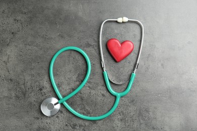 Photo of Cardiology. Stethoscope and red decorative heart on gray textured background, flat lay