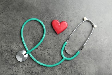 Photo of Cardiology. Stethoscope and red decorative heart on gray textured background, flat lay