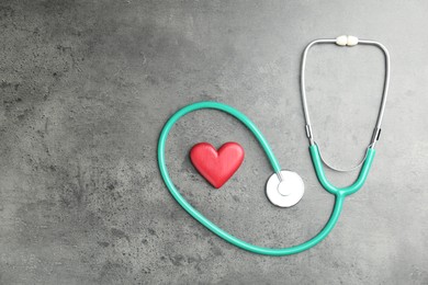 Photo of Cardiology. Stethoscope and red decorative heart on gray textured background, flat lay. Space for text