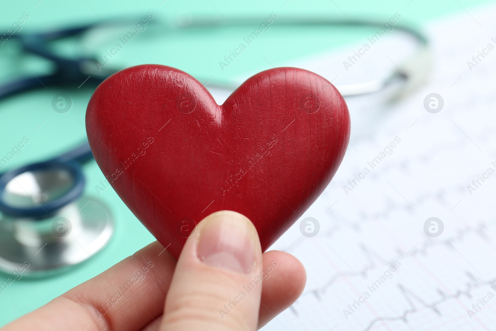 Photo of Cardiology. Woman with red decorative heart at table, closeup