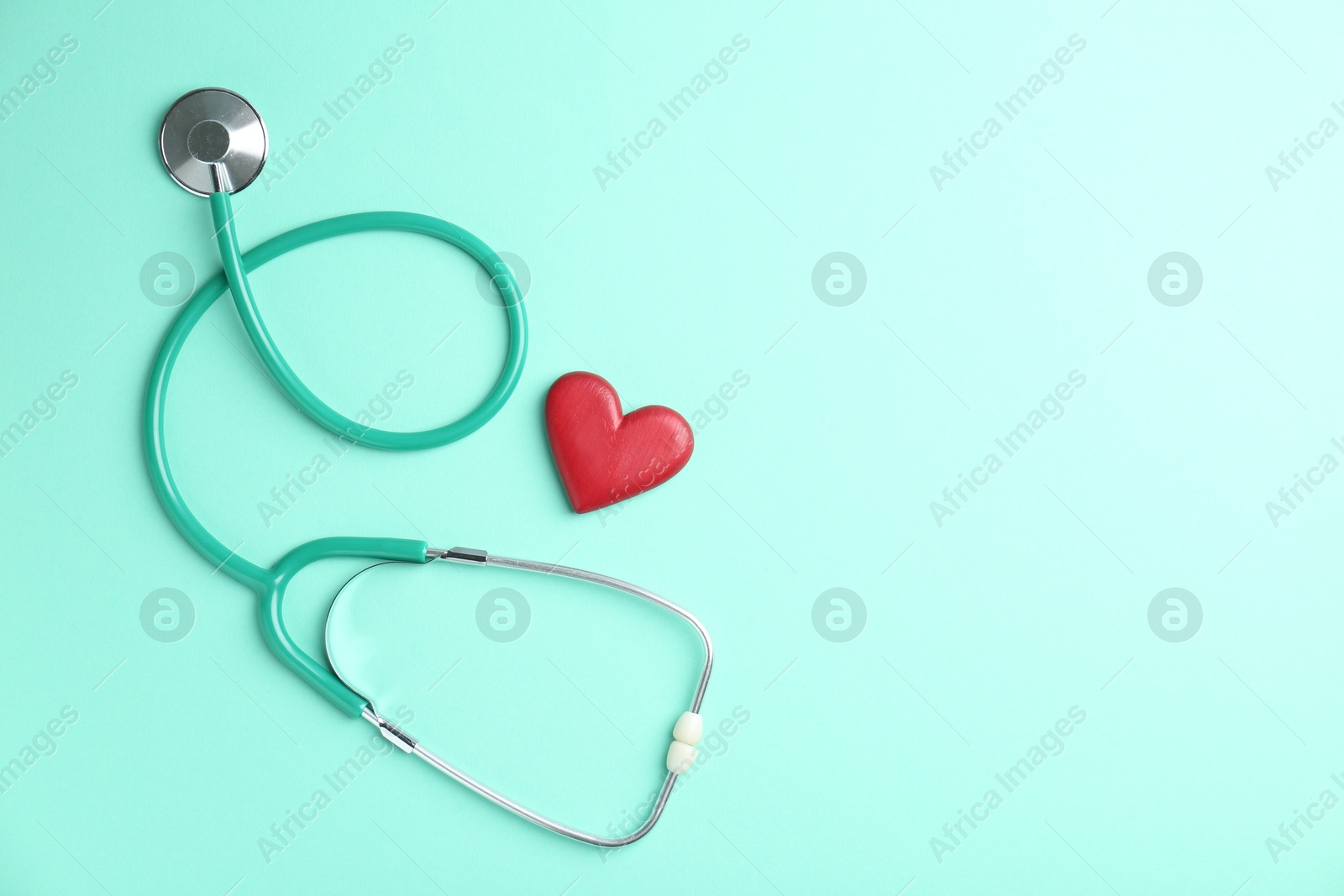 Photo of Cardiology. Stethoscope and red decorative heart on turquoise background, flat lay. Space for text