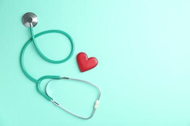 Photo of Cardiology. Stethoscope and red decorative heart on turquoise background, flat lay. Space for text