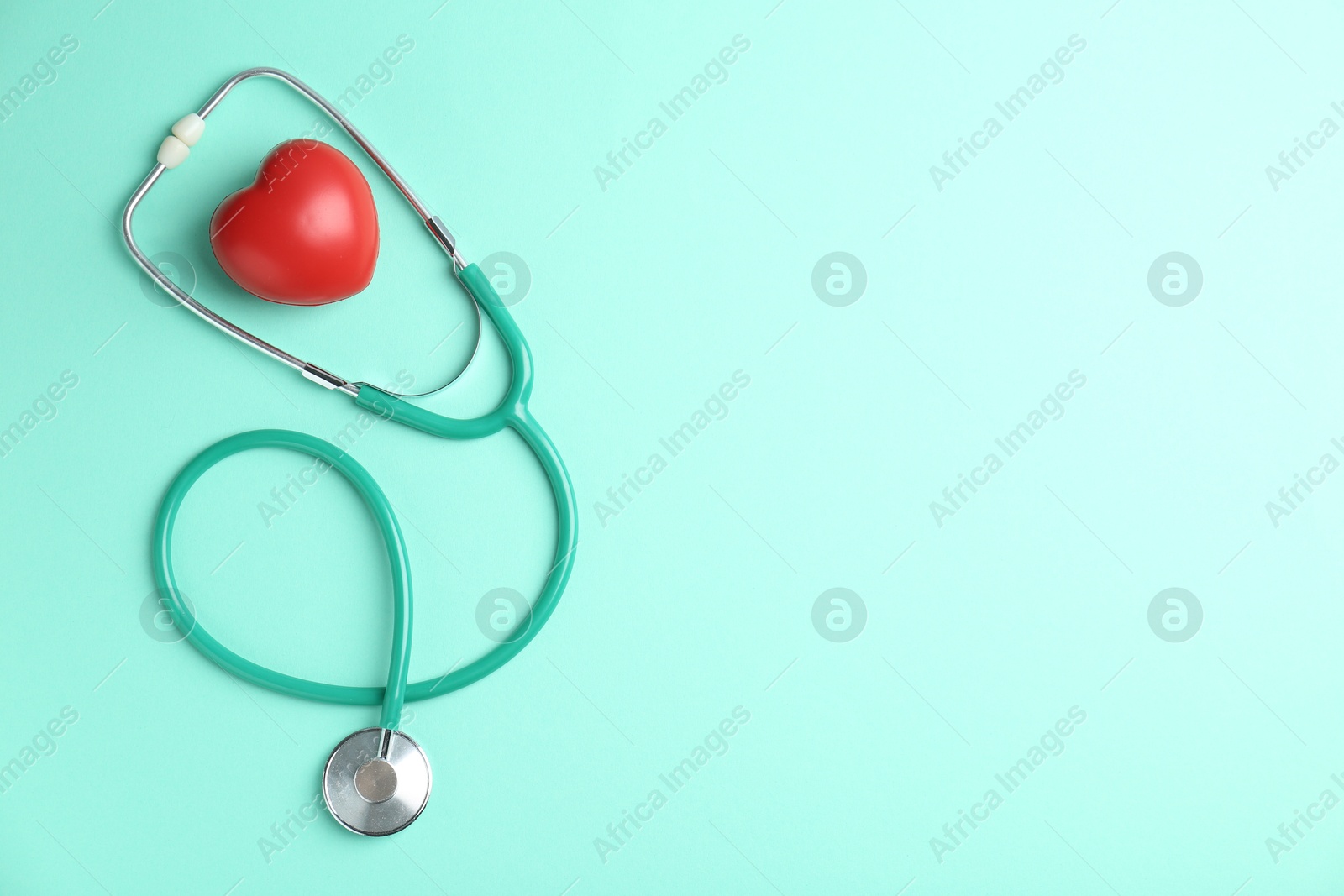 Photo of Cardiology. Stethoscope and red decorative heart on turquoise background, flat lay. Space for text