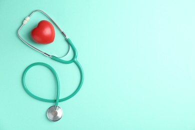 Photo of Cardiology. Stethoscope and red decorative heart on turquoise background, flat lay. Space for text