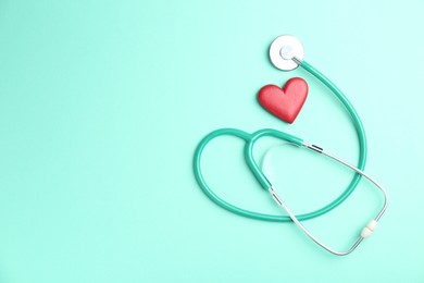 Photo of Cardiology. Stethoscope and red decorative heart on turquoise background, flat lay. Space for text