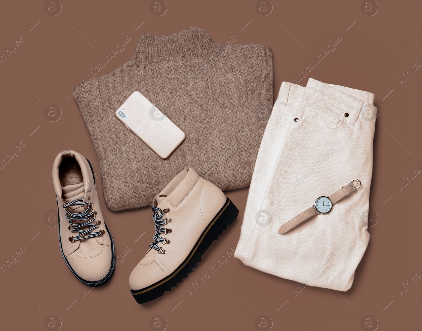 Image of Stylish boots, clothes, smartphone and wristwatch on mocha mousse shade background, flat lay. Trendy color of 2025 year