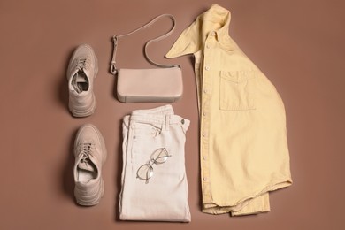 Image of Stylish outfit with bag on mocha mousse shade background, flat lay. Trendy color of 2025 year