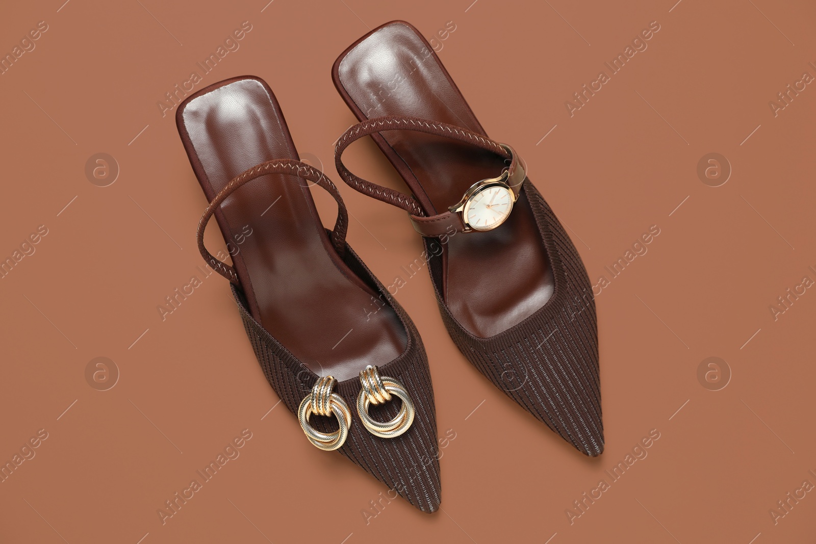 Image of Stylish women's shoes in mocha mousse shade, golden earrings and wristwatch on light brown background, top view. Trendy color of 2025 year